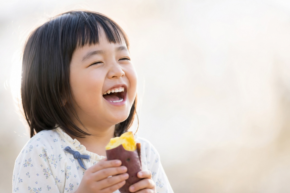 焼き芋を笑顔で食べている健康な歯の子ども